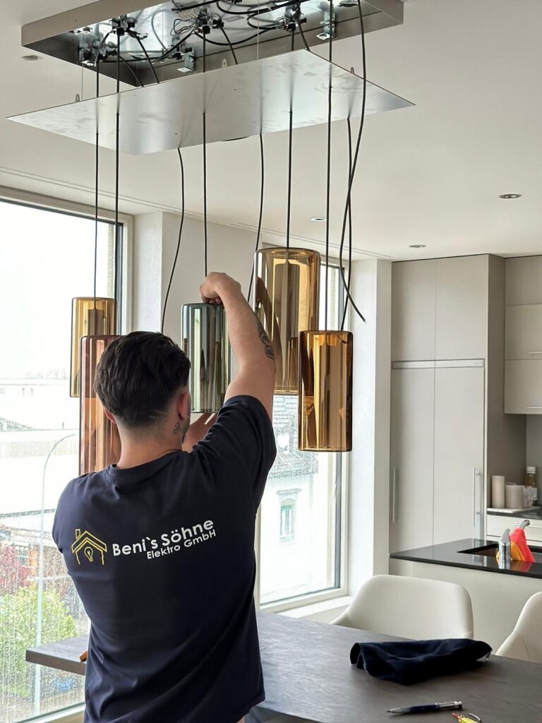 Elektriker von Beni's Söhne Elektro GmbH montiert Pendelleuchten über einer Kücheninsel
